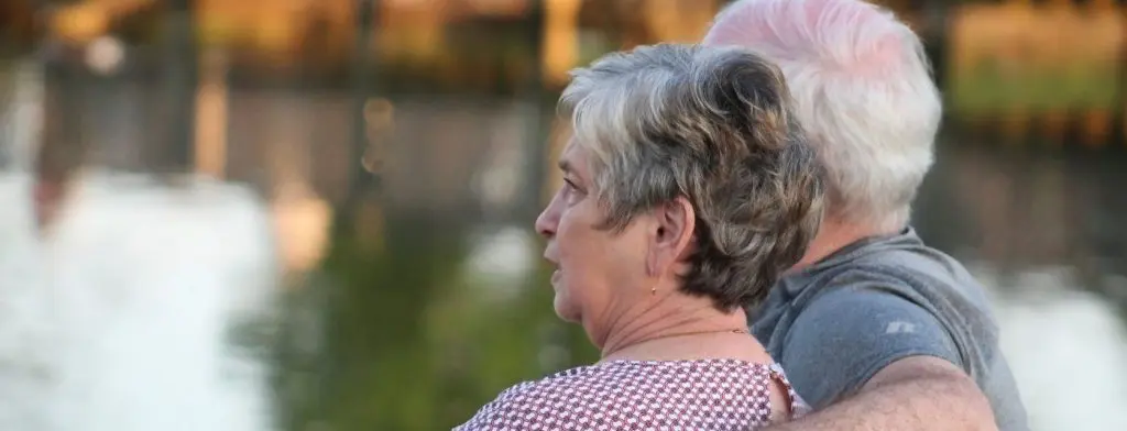 elderly couple sitting on bench by water