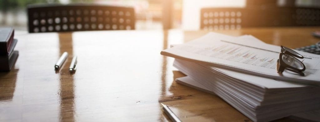 stack of paperwork with pens and glasses on a table