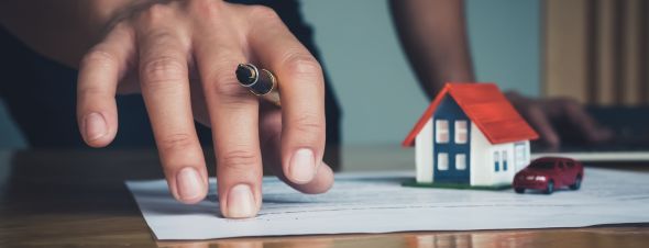hand pointing at paperwork with model house and car